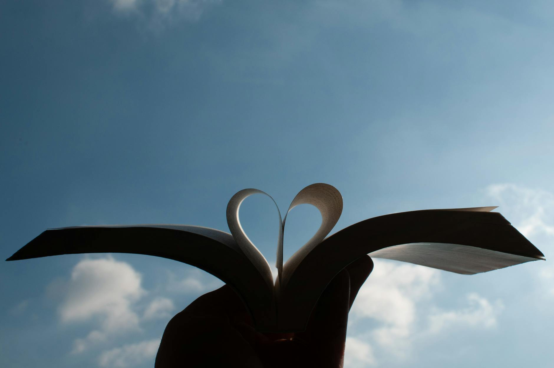 open book forming heart shape against blue sky